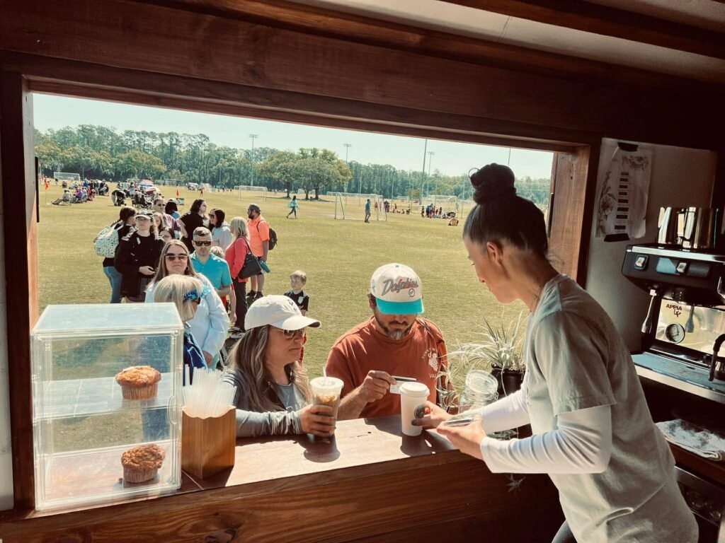 Jacqui serving handcrafted coffee from her trailer window to customers at a Clay County soccer field