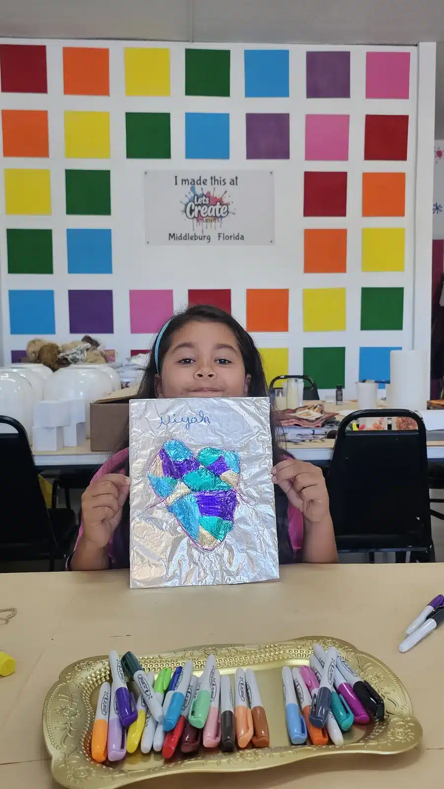 Young artist showing a foil heart art project at Let's Create Studios in Middleburg