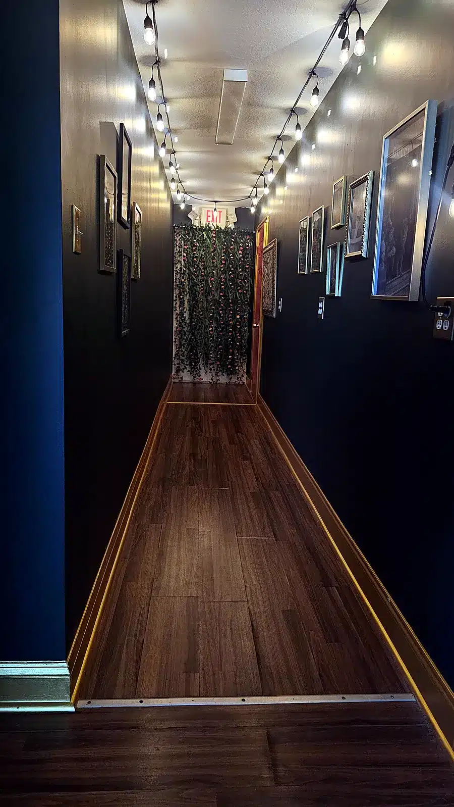 Hallway with string lights, gallery wall and dark green walls inside Massage Craving in Green Cove Springs