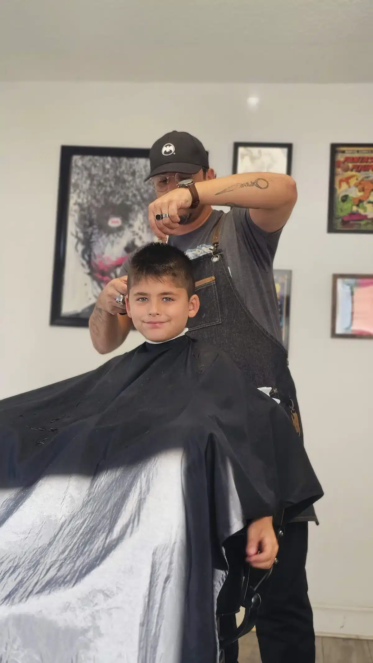 Jay works on a young client's haircut in front of framed comic book art at Intermissions Barbershop
