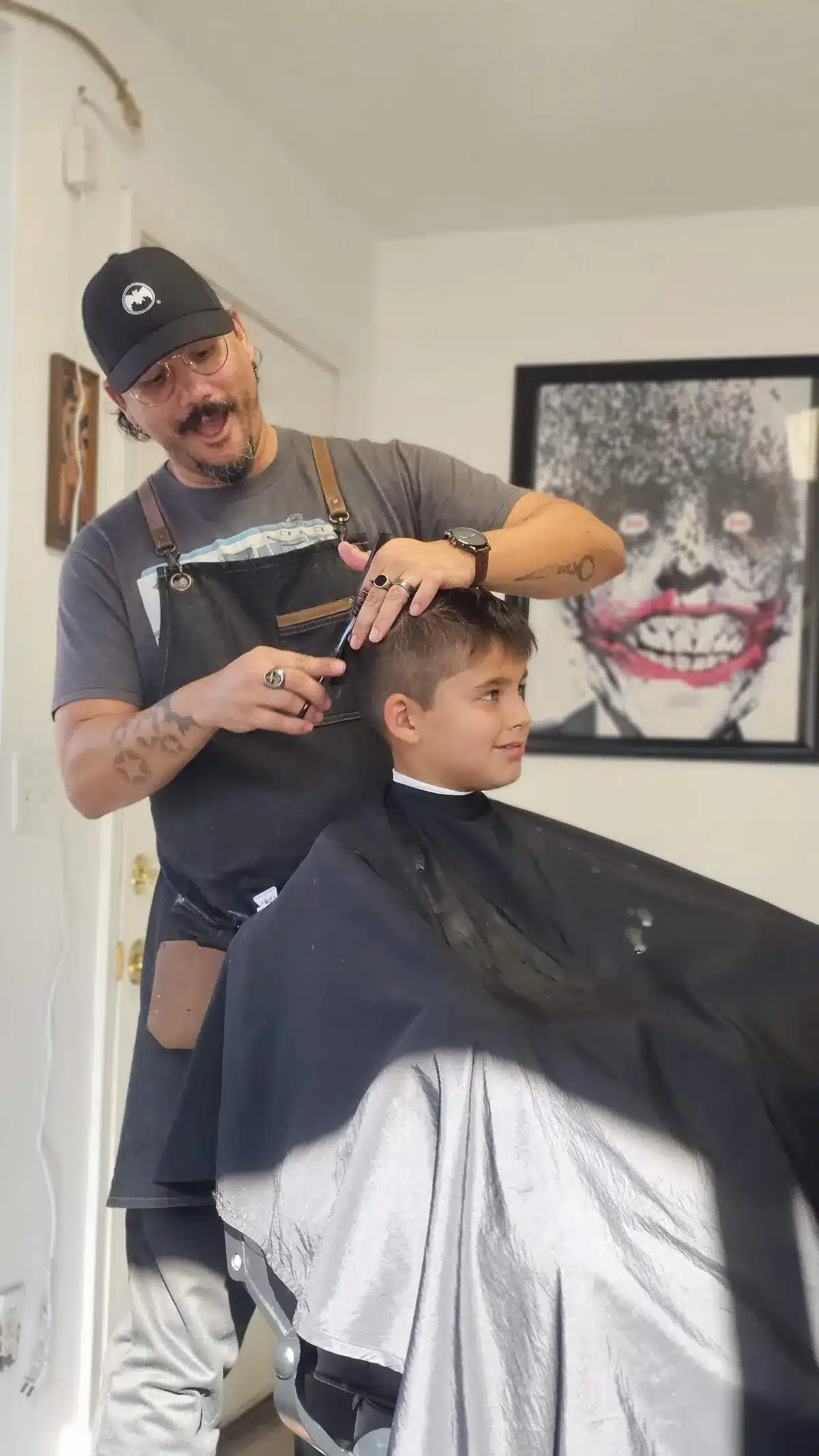 Jay laughing and talking with a young boy while trimming his hair with scissors and a comb